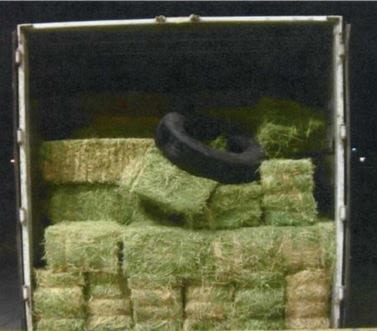 A truck with an open back filled with hay bails and a tire